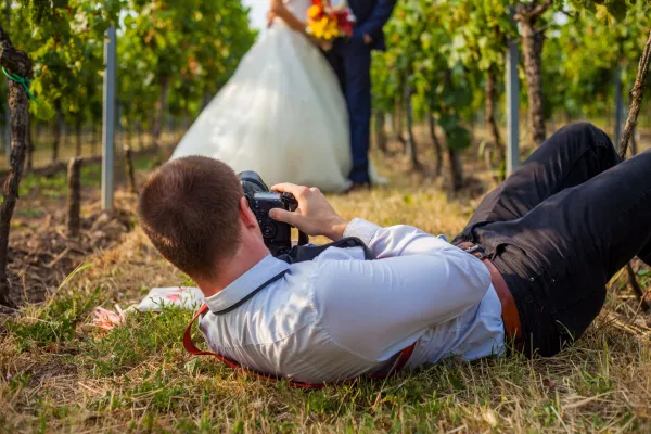 Fotografie de nuntă: Fotograf de nuntă întins pe o pajiște pentru a fotografia un cuplu de miri.